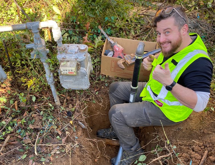 Plumber in a safety vest repairing an outdoor water meter connection
